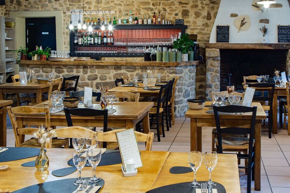 Intérieur du restaurant avec tables et bar en bois, murs en pierre et cheminée.