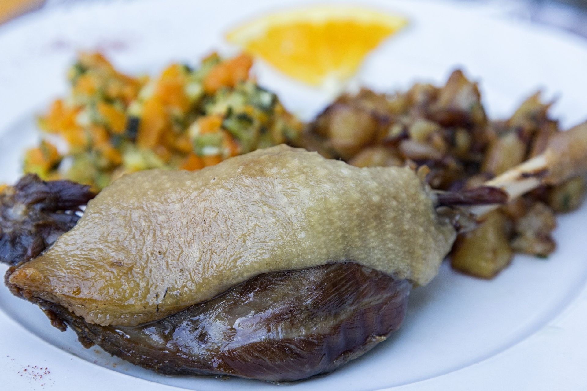 Cuisse de canard confite avec pommes de terre rôties et salade d'accompagnement, servie sur une assiette blanche.
