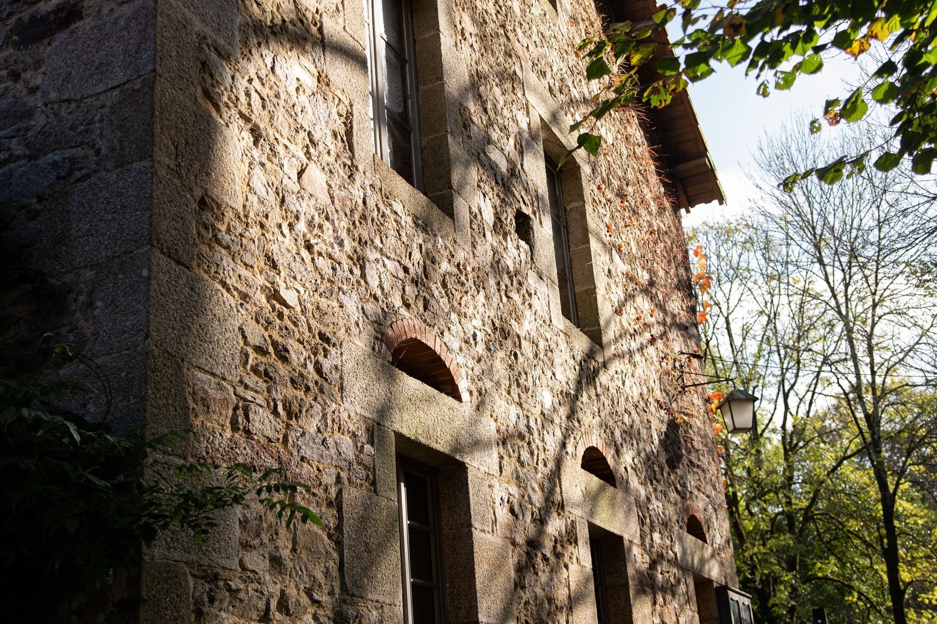 Bâtiment en pierre à l'extérieur, ombragé par des arbres, avec des fenêtres et des arcades.