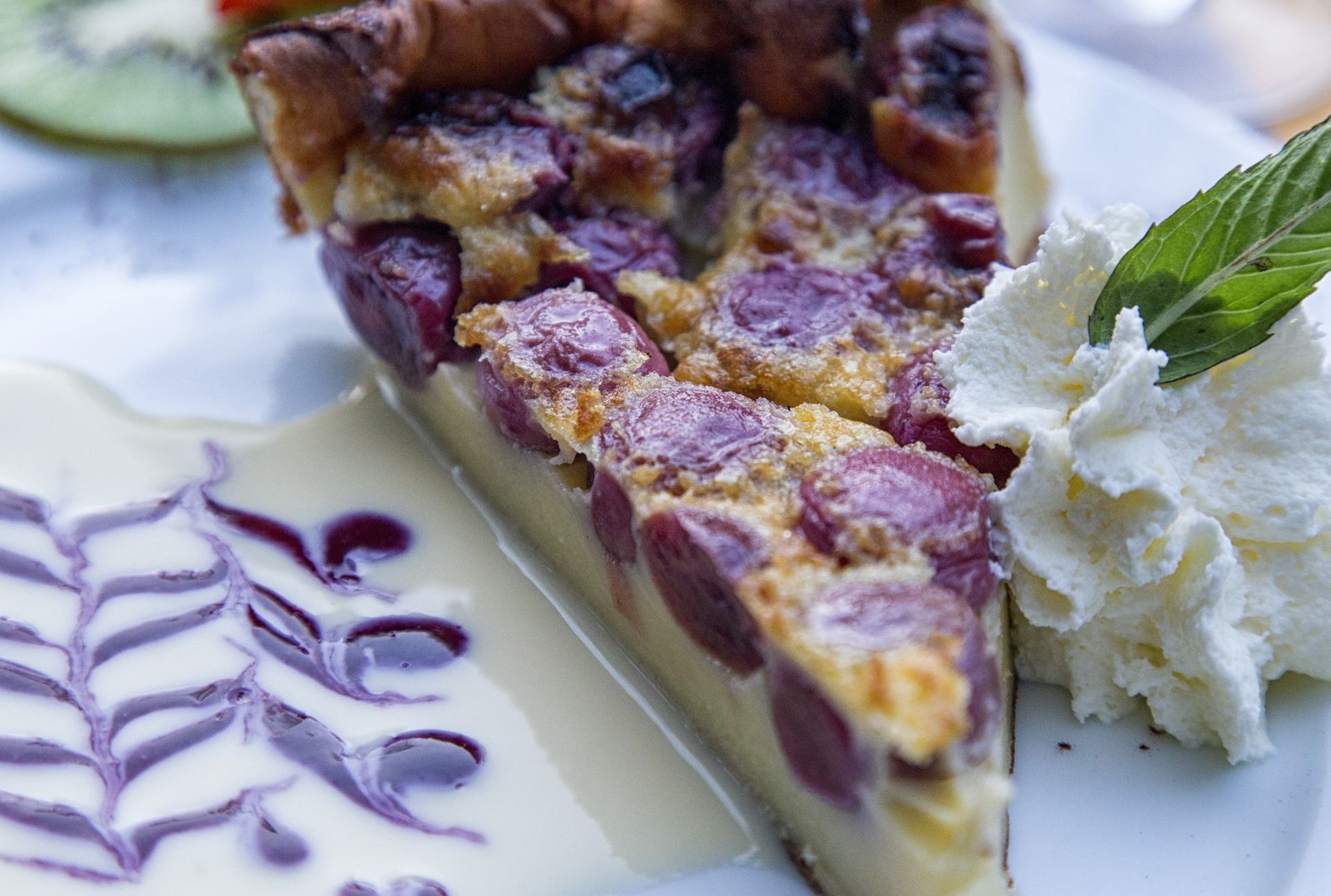Tranche de clafoutis aux cerises avec crème fouettée et sauce, servie sur une assiette blanche.
