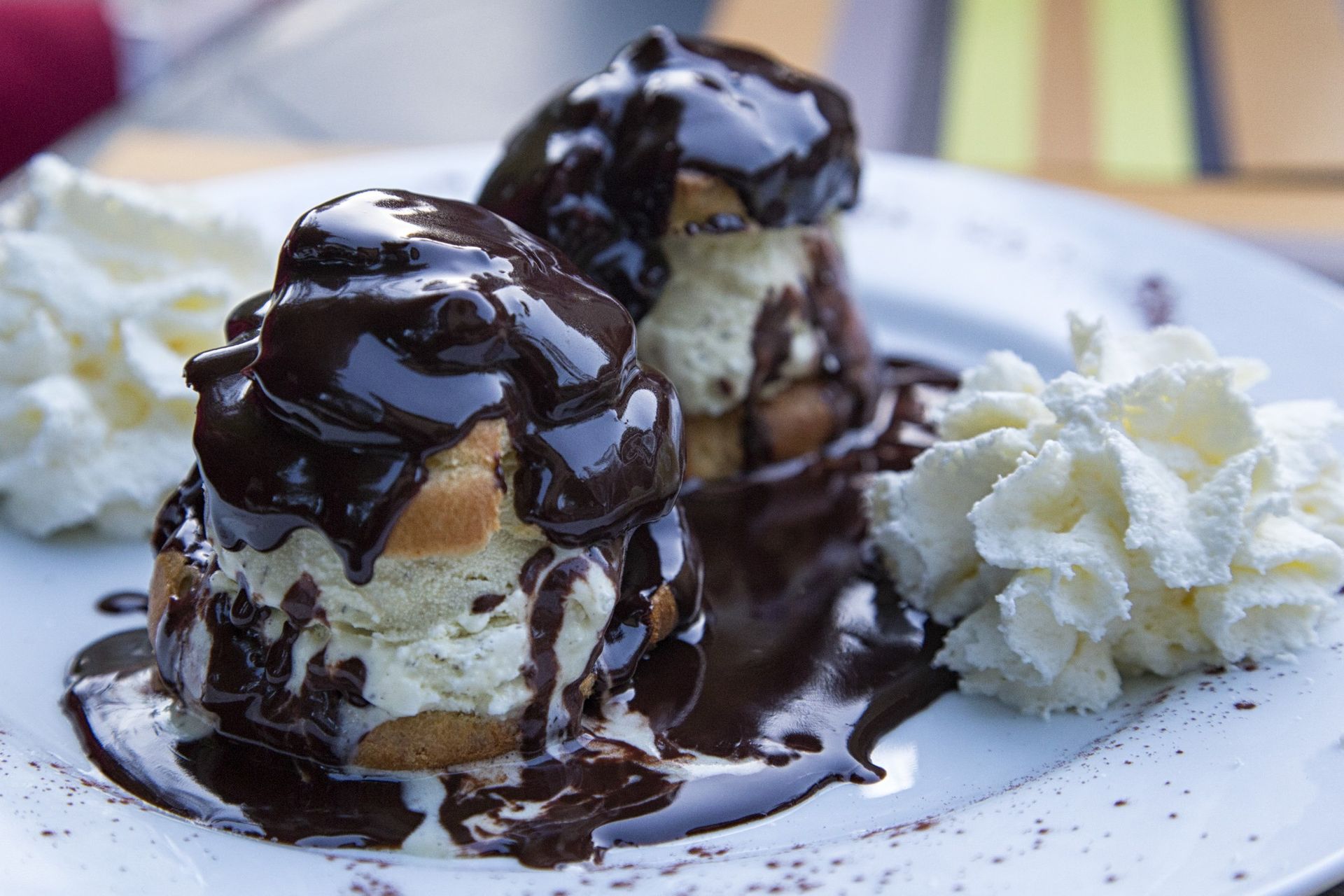Choux à la crème enrobés de chocolat, accompagnés de crème fouettée, présentés sur une assiette blanche.