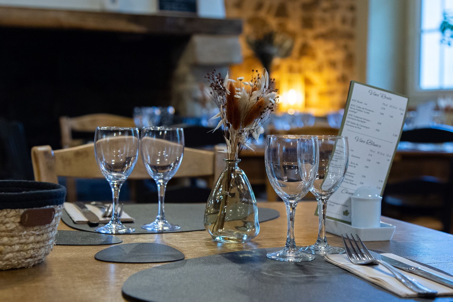 Table de restaurant dressée avec des verres à vin, un vase de fleurs et un menu.