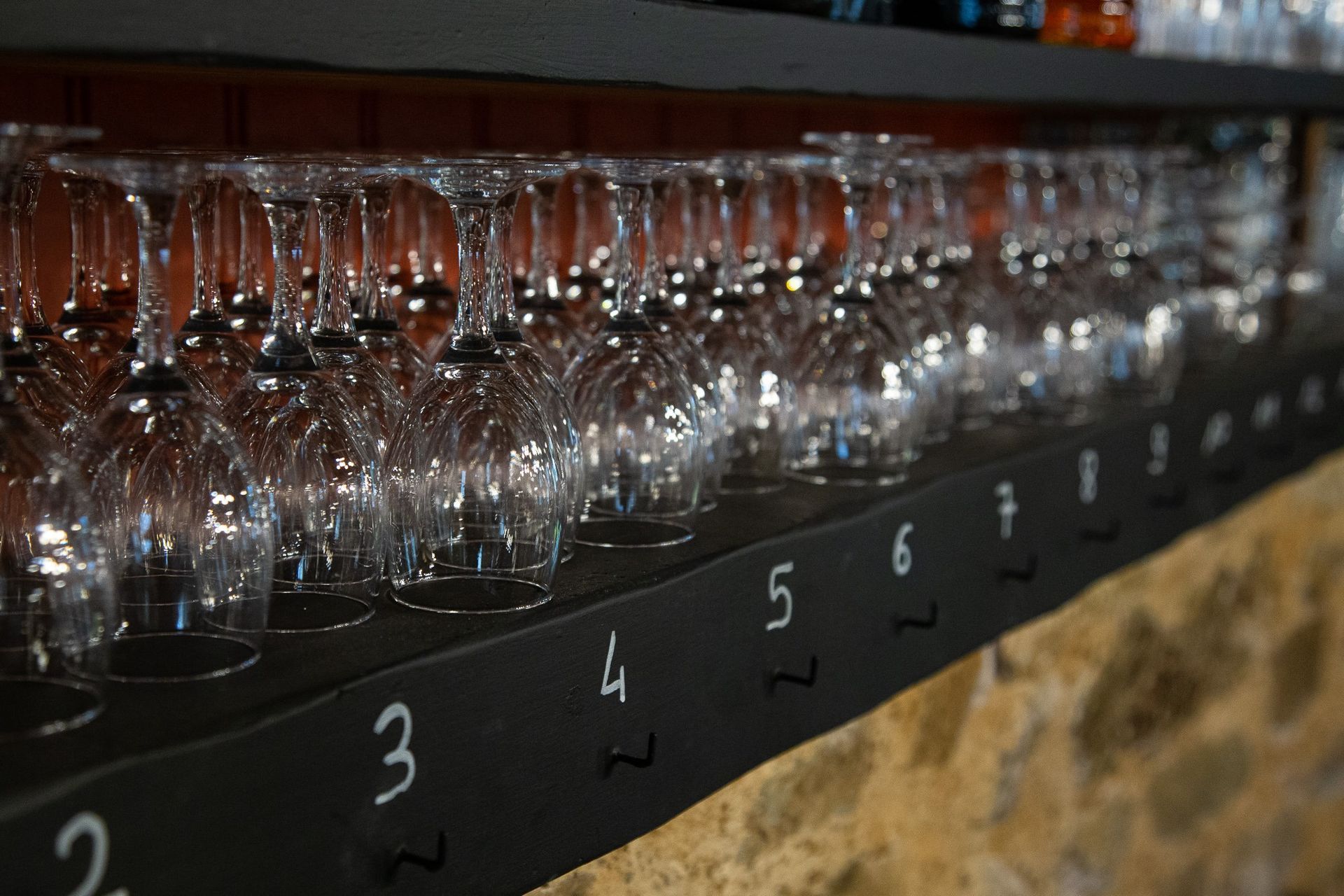 Des verres à vin alignés sur une étagère numérotée dans un bar.
