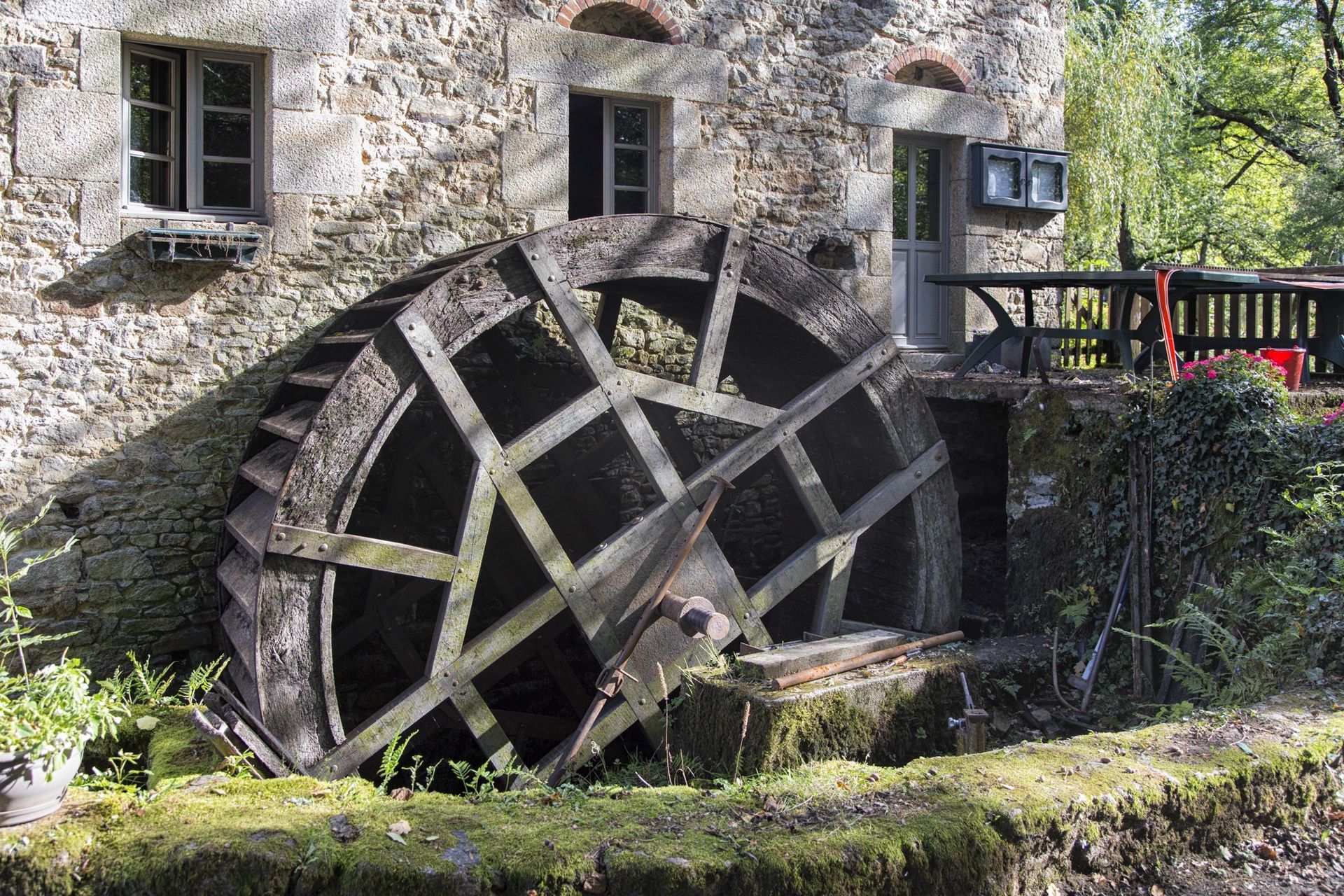 Roue à eau d'un ancien moulin en pierre, avec fenêtres, porte et petit coin salon extérieur.