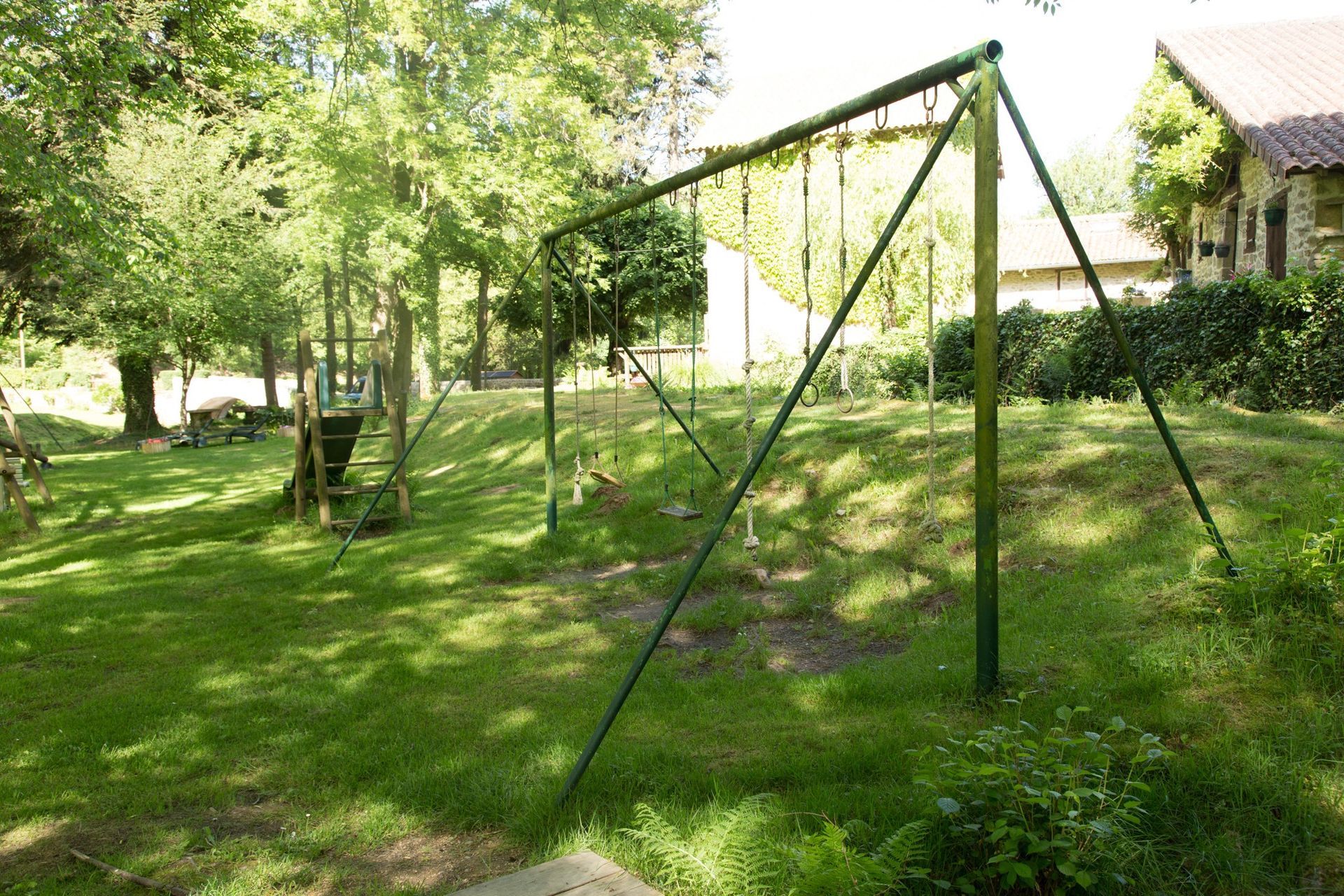 Balançoire verte sur une colline herbeuse dans un parc, avec des arbres et un bâtiment en arrière-plan.