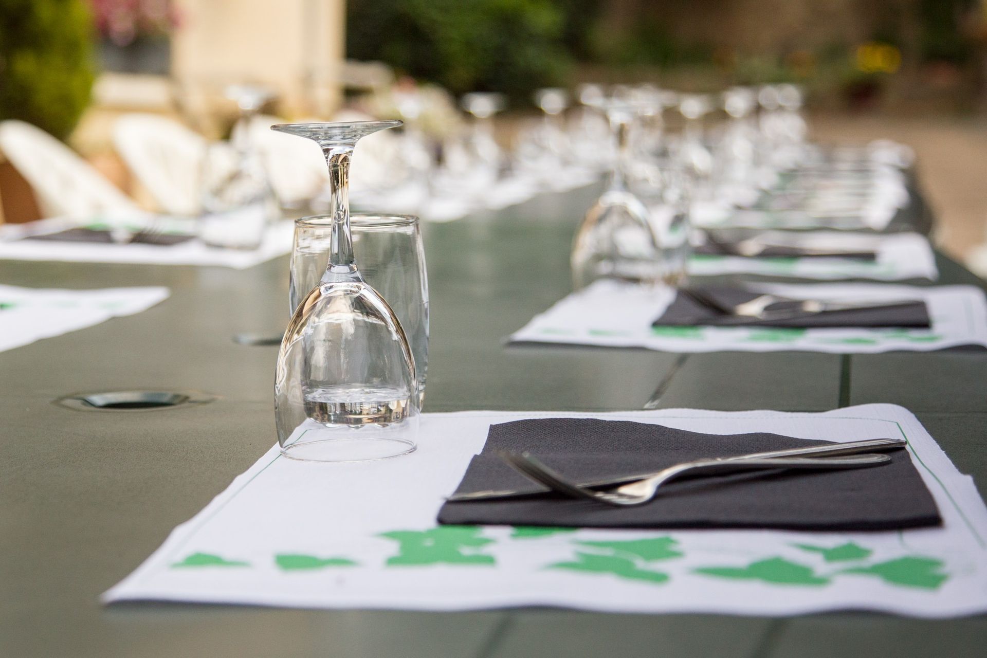 Longue table dressée à l'extérieur avec verres à vin, couverts, serviettes et sets de table.