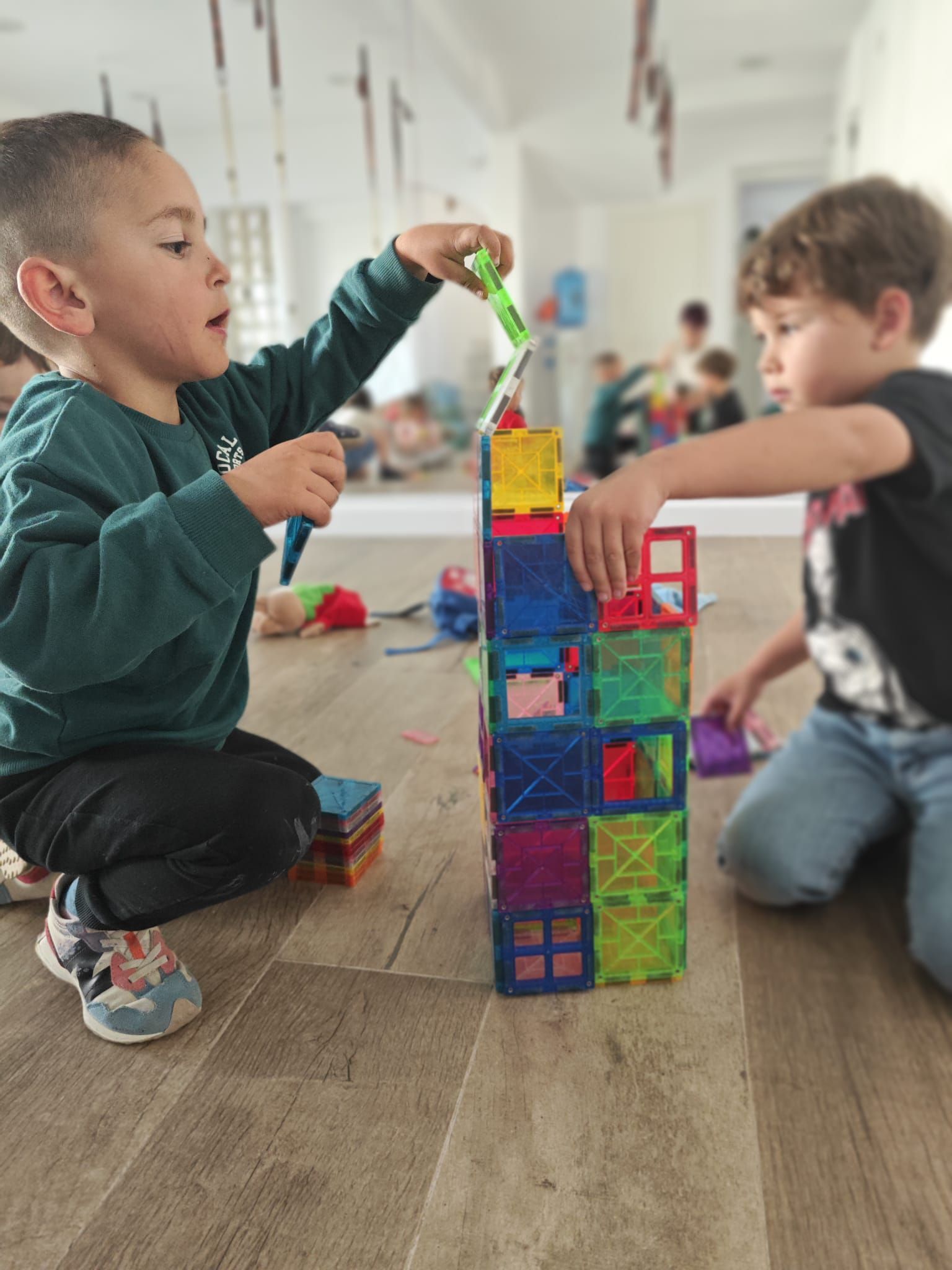Dos niños pequeños están jugando con bloques magnéticos en el suelo.