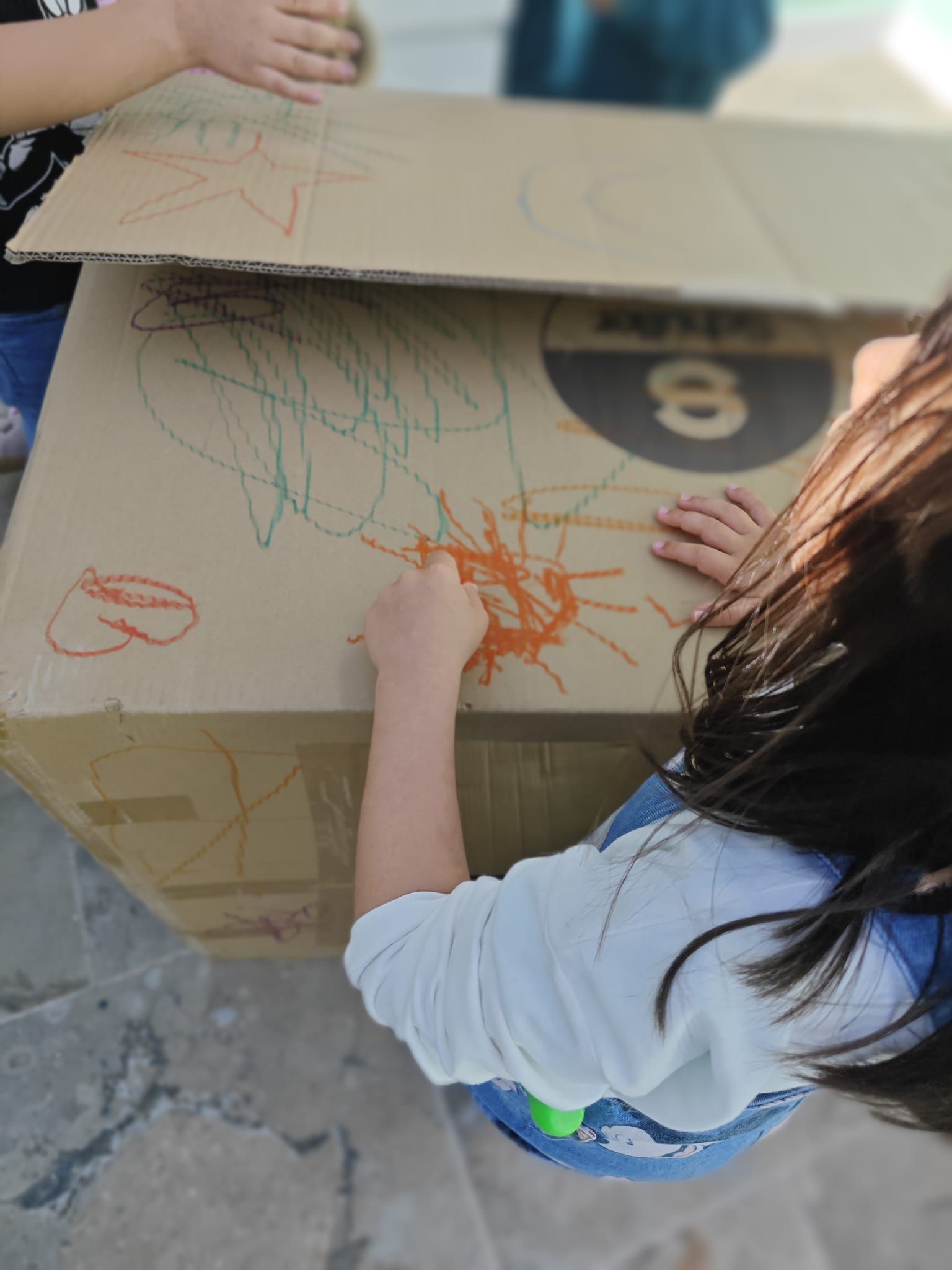 Una niña está dibujando en una caja de cartón.