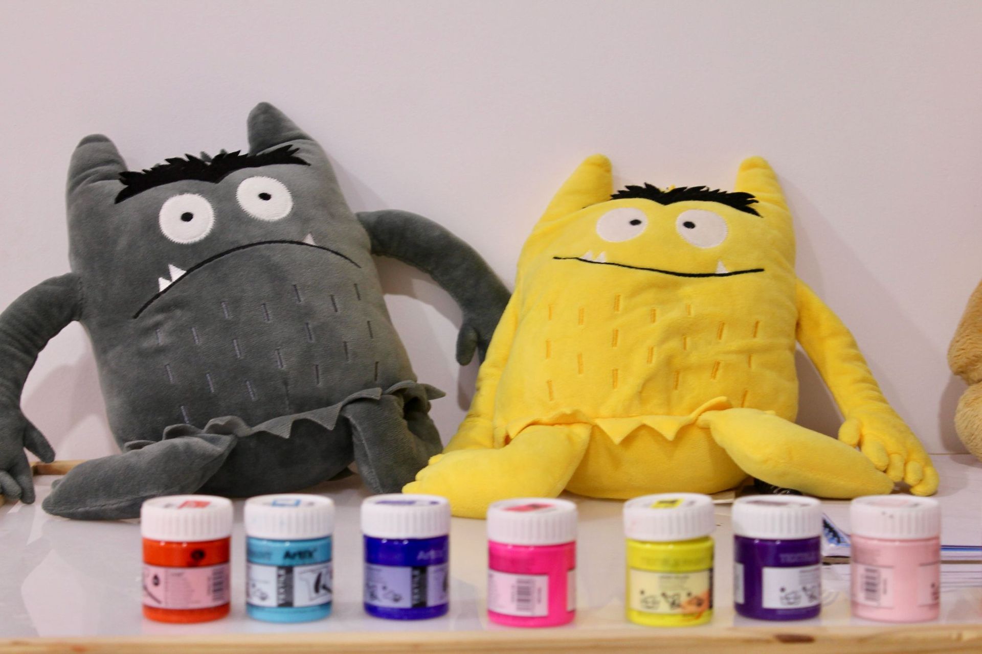 Dos monstruos de peluche están sentados junto a botellas de pintura.