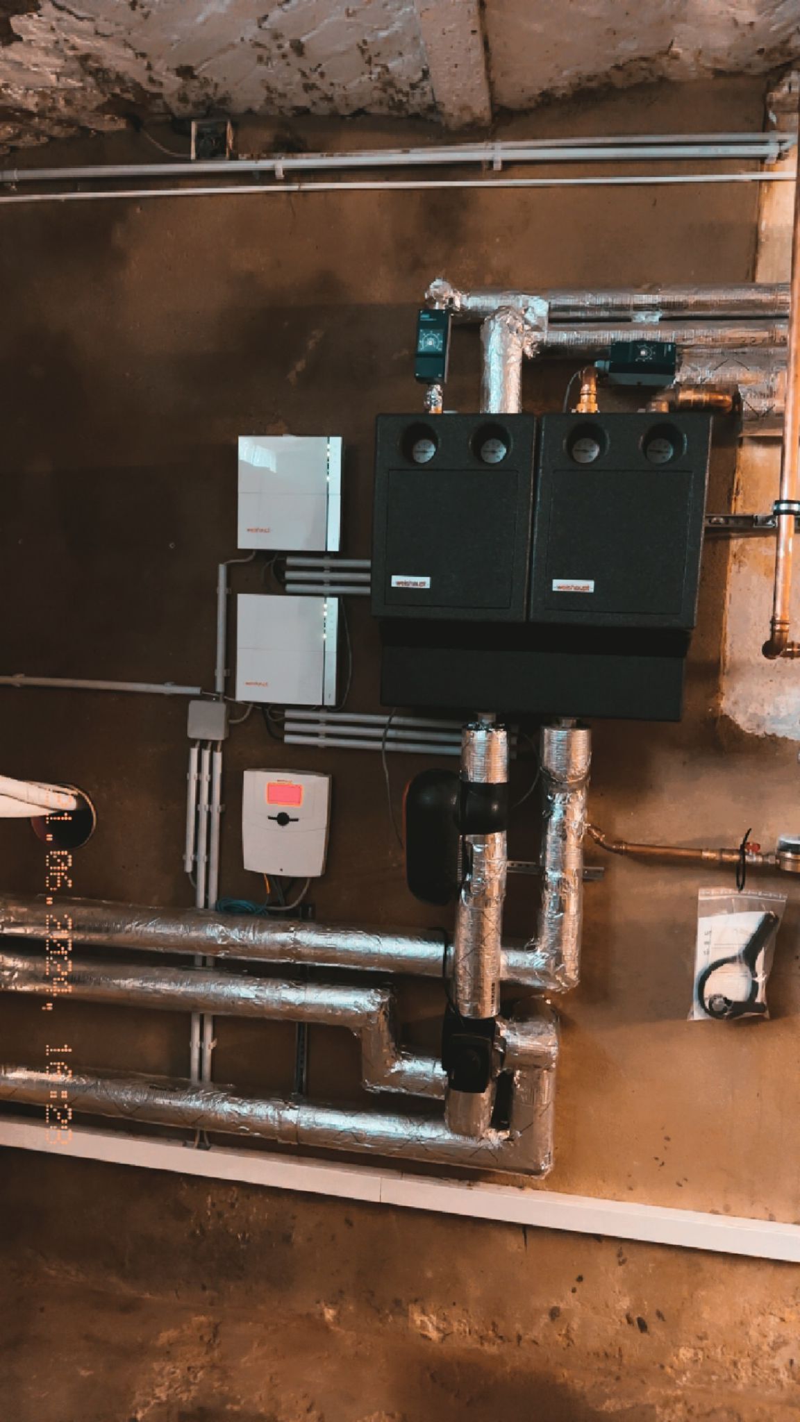 Sanitär- und Elektrogeräte an einer braunen Wand: Rohre, Kästen und Kabel.