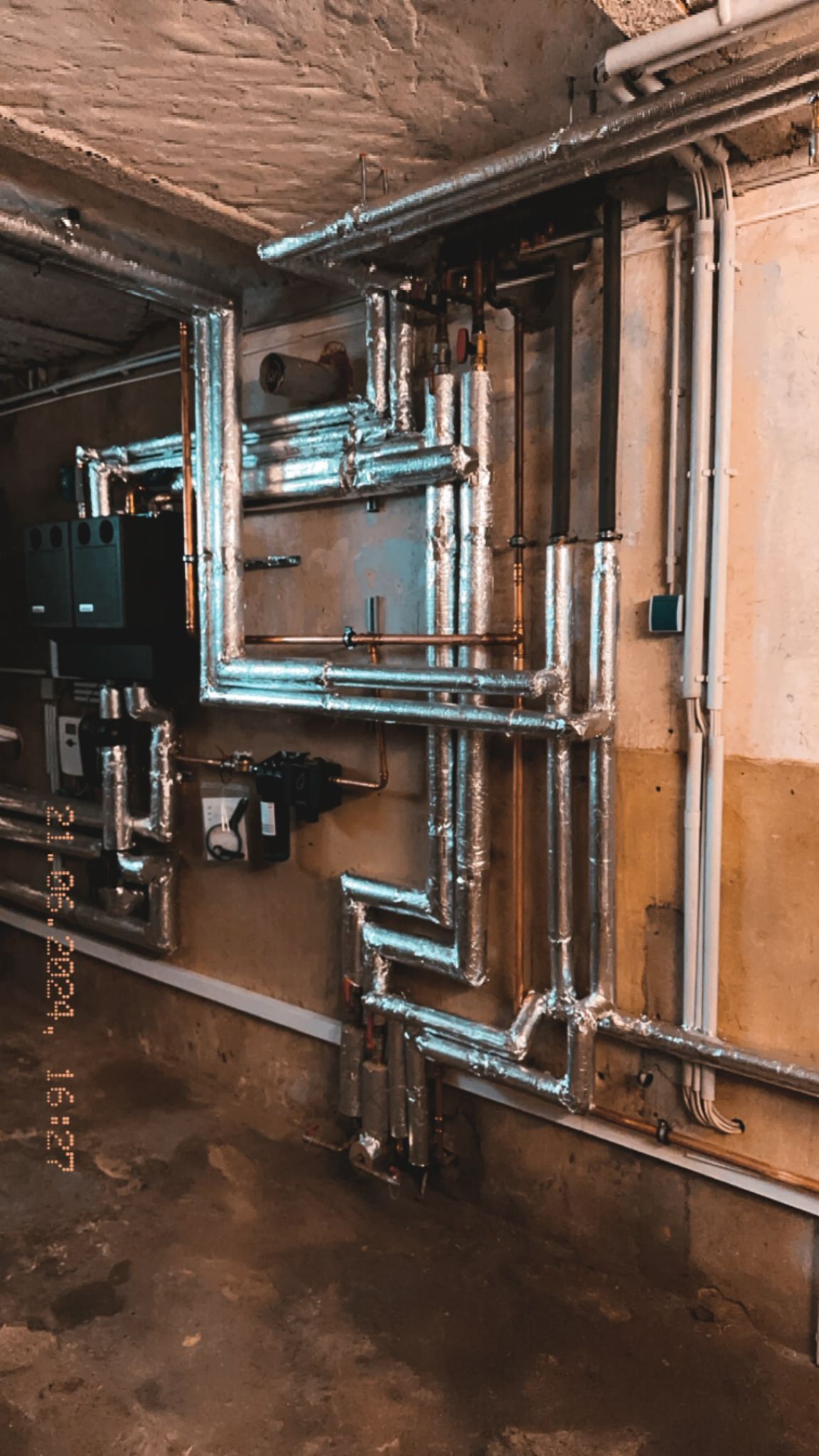 Keller mit Industrierohren und -geräten, möglicherweise ein Hauswirtschaftsraum. Silberne Isolierung, Betonwände.