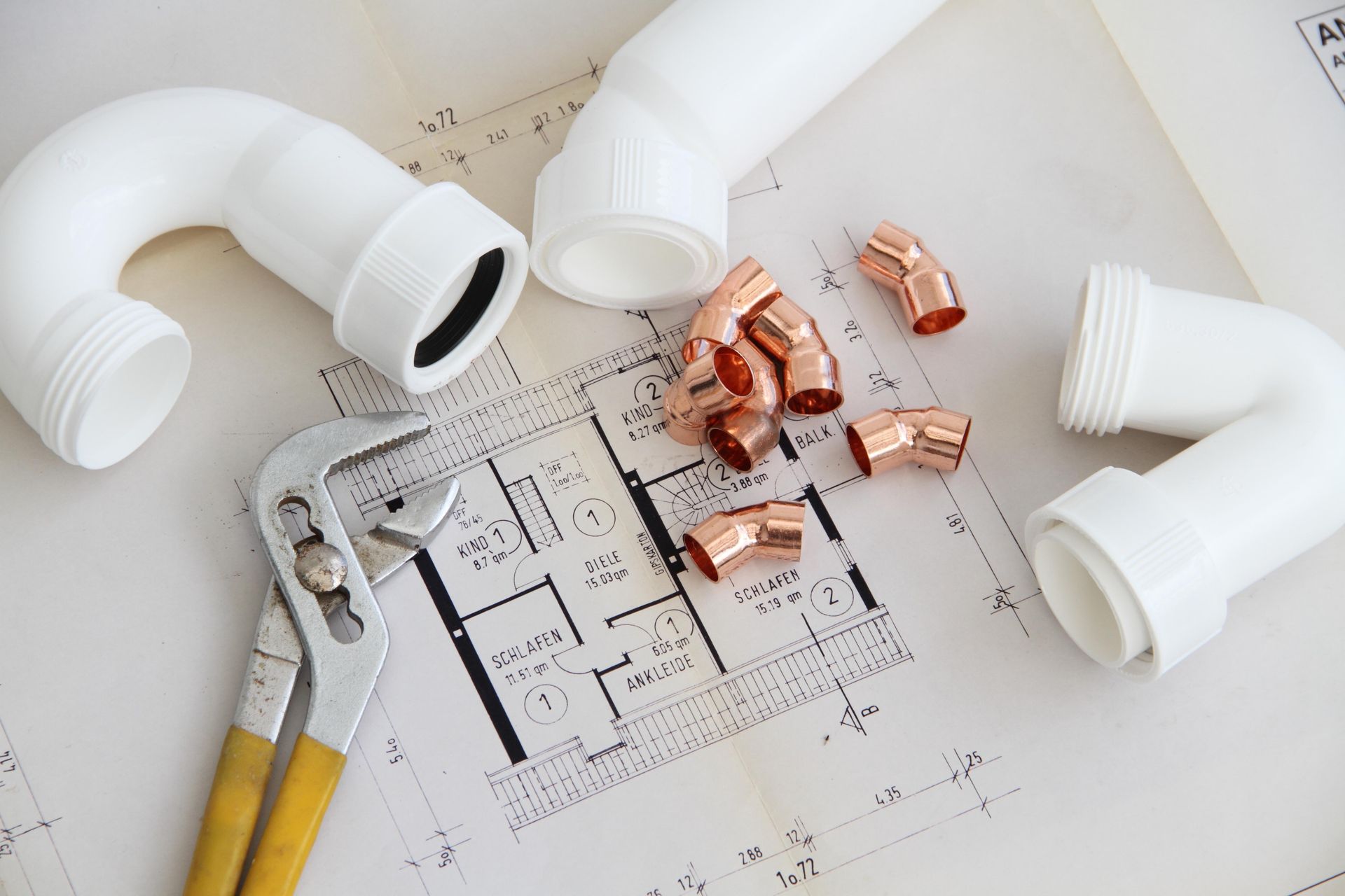Sanitärwerkzeuge, Rohre und Kupferverbindungen auf Bauplänen, die auf Bau oder Reparatur hinweisen.