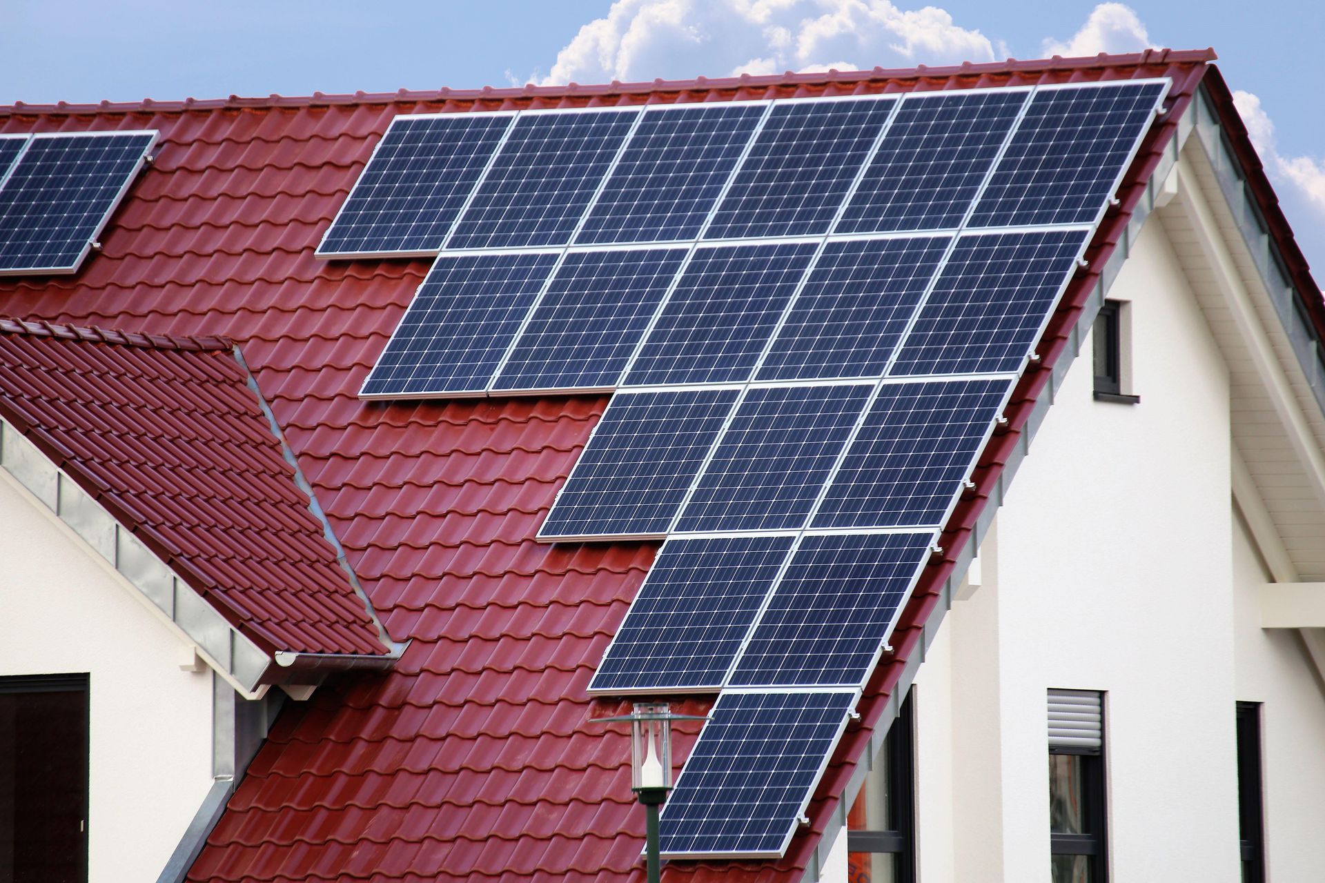 Auf dem roten Dach eines weißen Hauses sind Solarmodule installiert, die Sonnenlicht zur Energiegewinnung einfangen.