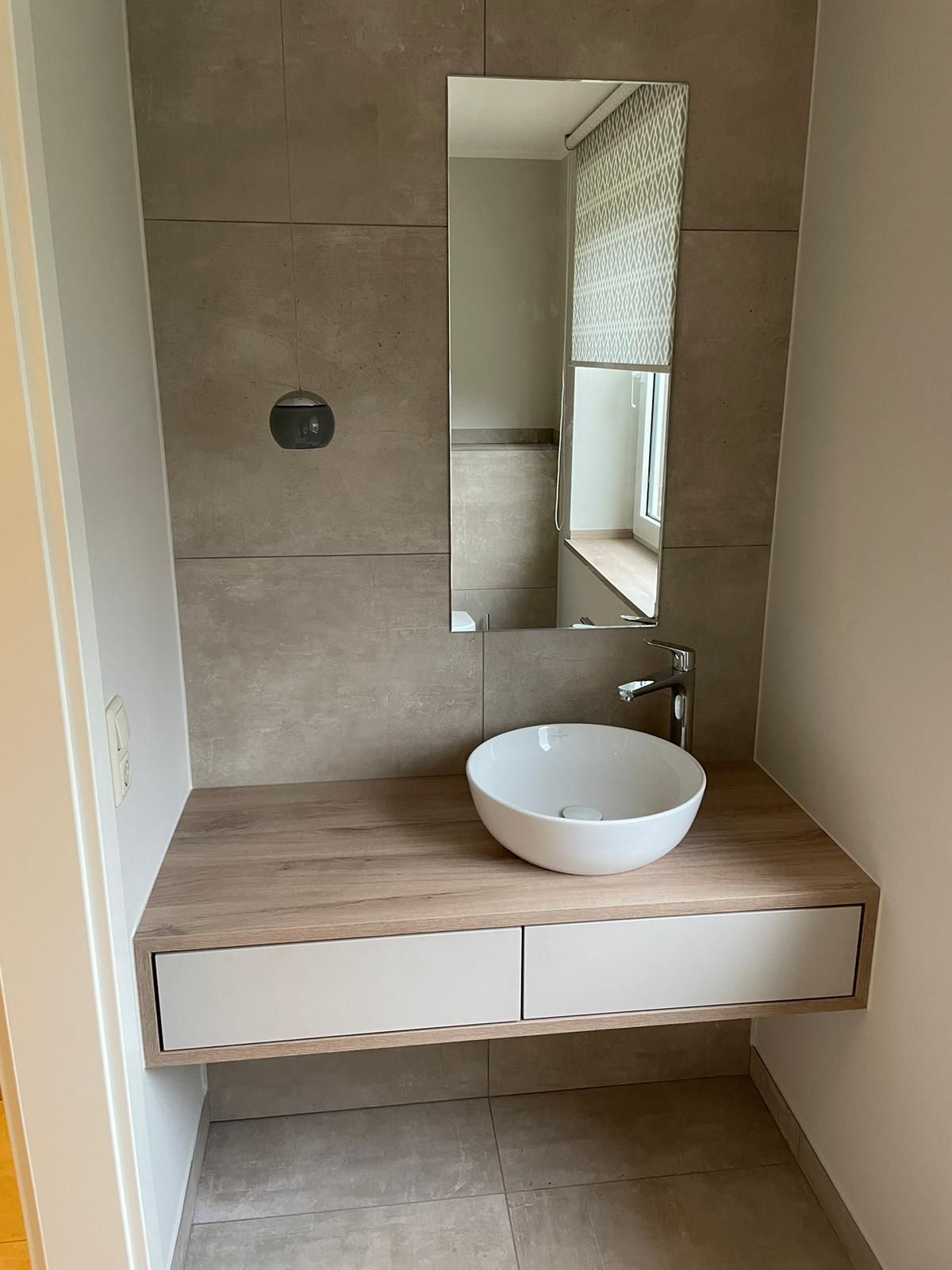 Ein modernes Badezimmerwaschbecken mit schwebendem Holzwaschtisch, einem weißen Aufsatzwaschbecken und einem rechteckigen Spiegel.