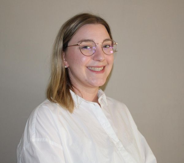 Frau mit Brille und weißem Hemd lächelt.