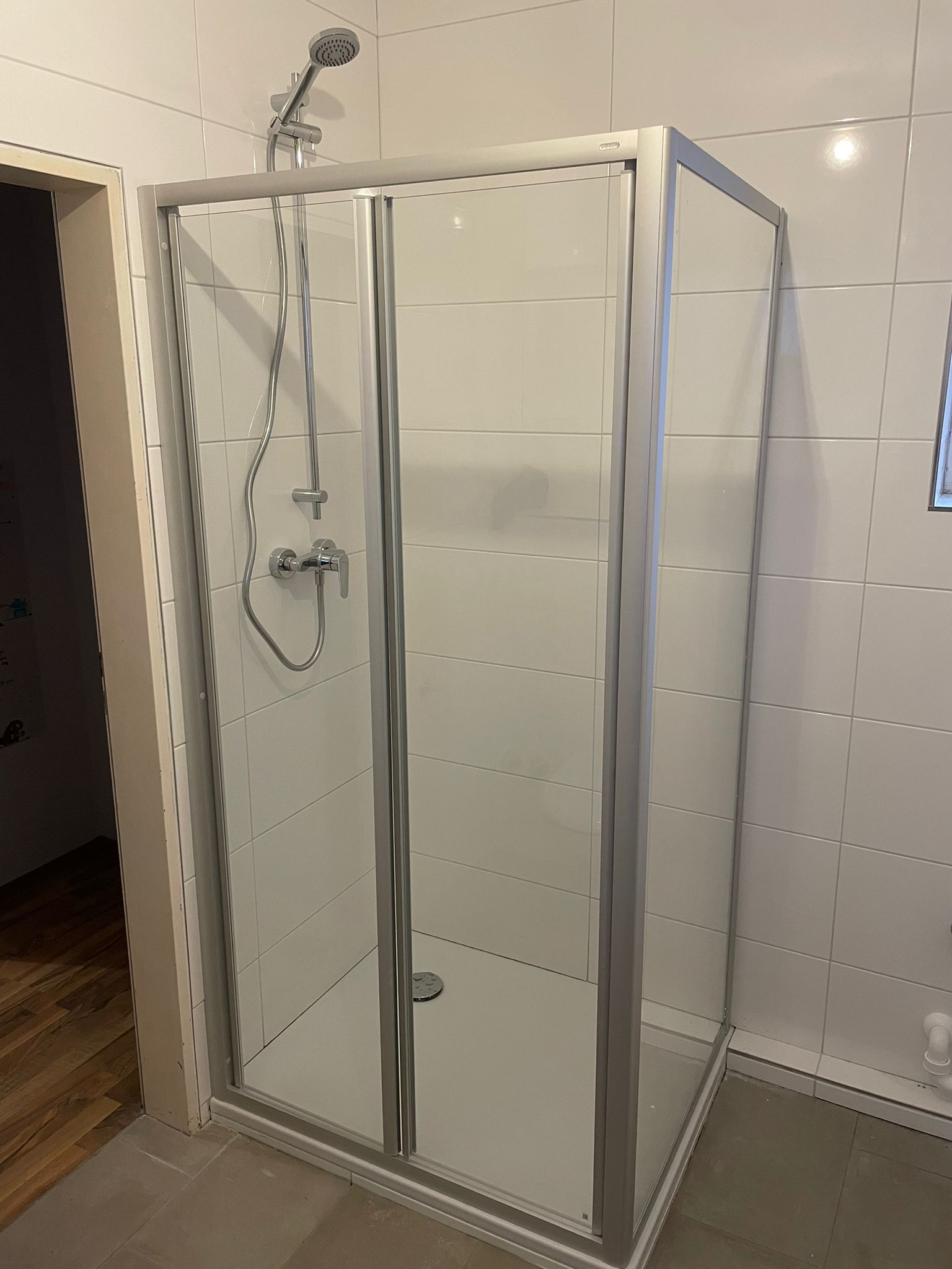 Duschkabine mit klaren Glastüren und silbernem Rahmen in einem weiß gefliesten Badezimmer.