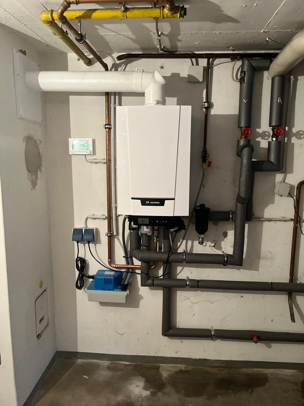 Ein weißer, an der Wand montierter Gaskessel mit Rohren in einem Keller.