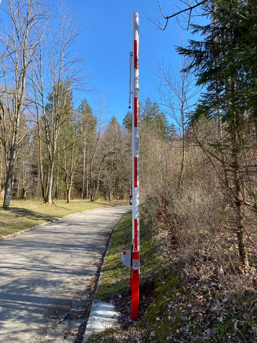 Hohe rot-weiß gestreifte Barriere auf einem Weg, die den Fahrzeugzugang in einem Waldgebiet blockiert.
