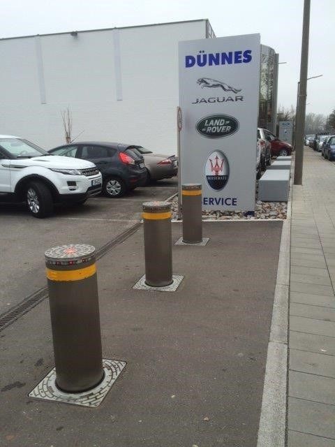 Braune Poller vor dem Schild eines Autohauses mit den Logos von Jaguar und Land Rover. Autos und Gebäude sind sichtbar.