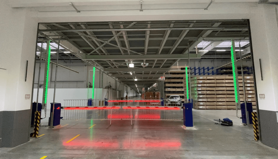 Ein Lagerhauseingang mit roten Laserstrahlen, grünen Pfosten und grauem Boden.