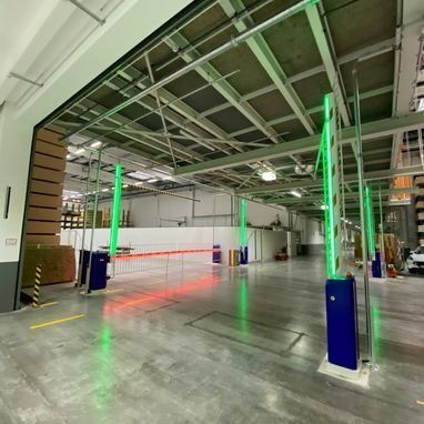 Grün-blaues Sicherheitstorsystem in einem Lagerhaus mit roter Beleuchtung und Metallstützen an der Decke.