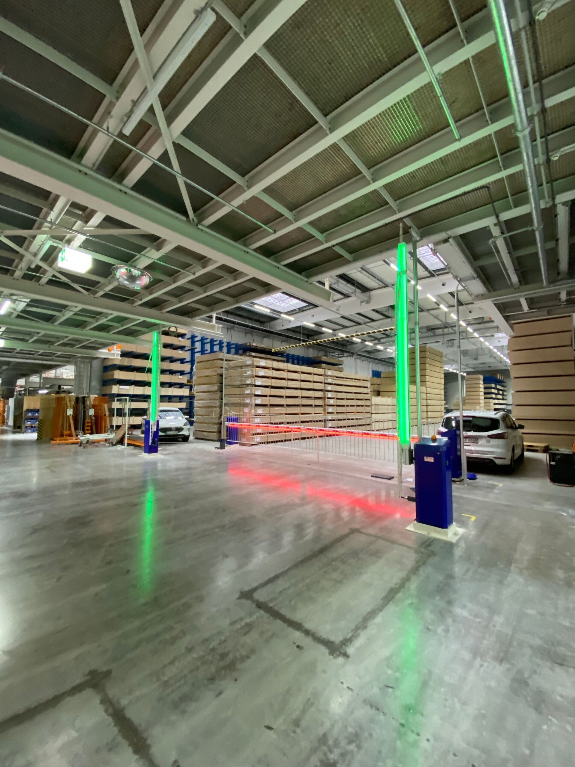 Ein Lager mit grünem und rotem Lasersicherheitssystem. Zwei Säulen strahlen grünes Licht und rote Laserstrahlen auf den Boden.