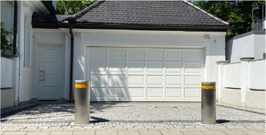Zwei graue Poller mit gelben Spitzen vor einer weißen Garage.