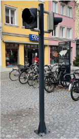 Ampel auf einem hohen Mast, im Hintergrund Gebäude und geparkte Fahrräder.
