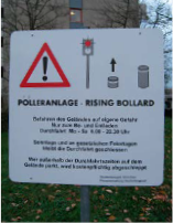 Schild für einen hochfahrbaren Poller mit Warnsymbol und Hinweisen. Er steht in einer Rasenfläche.