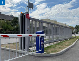 Schiebesicherheitstor mit Schrankenbaum an der Einfahrt zu einem Parkplatz. Graues Metall, blauer Kiosk, rot-weiß gestreifter Arm.