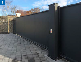 Schwarzes Schiebetor auf Ziegelpflaster, eine Säule mit Bedienfeld und links eine Steinmauer.