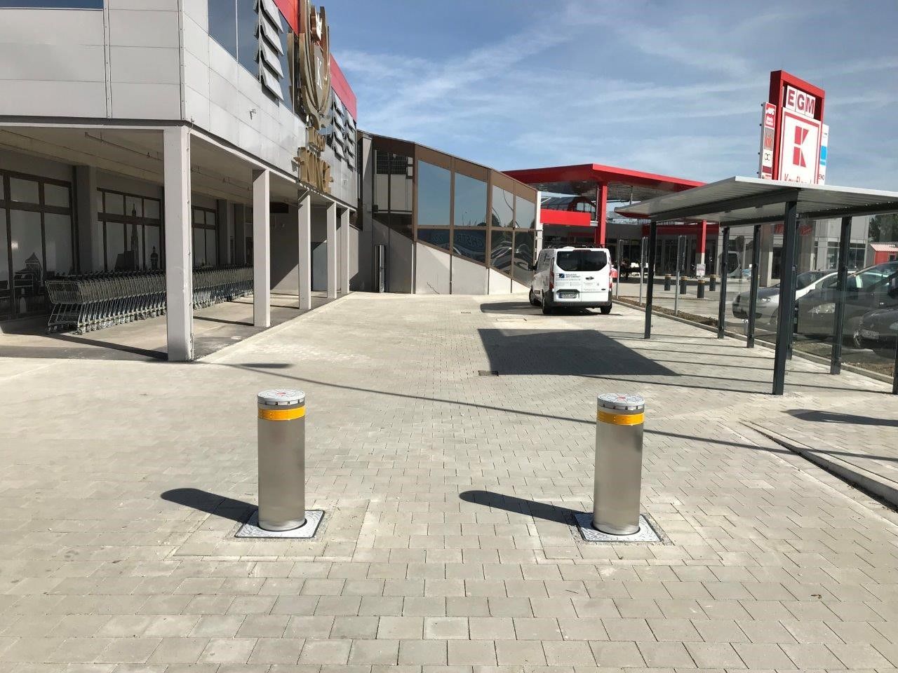 Außenansicht eines Gebäudes mit Pollern am Eingang, einem geparkten weißen Lieferwagen und einem blauen Himmel darüber.