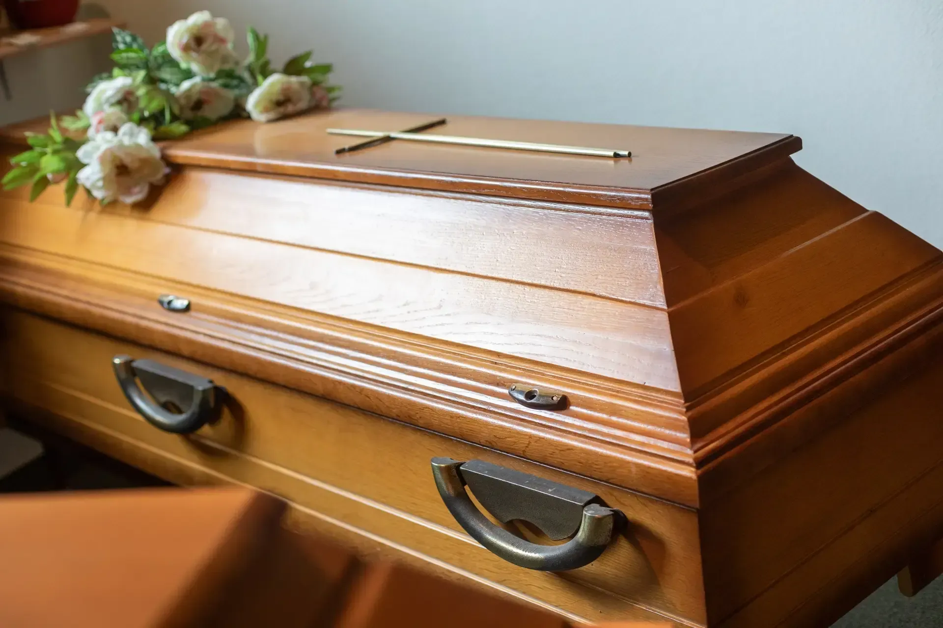 Ein Holzsarg mit Blumen darauf in einem Raum.