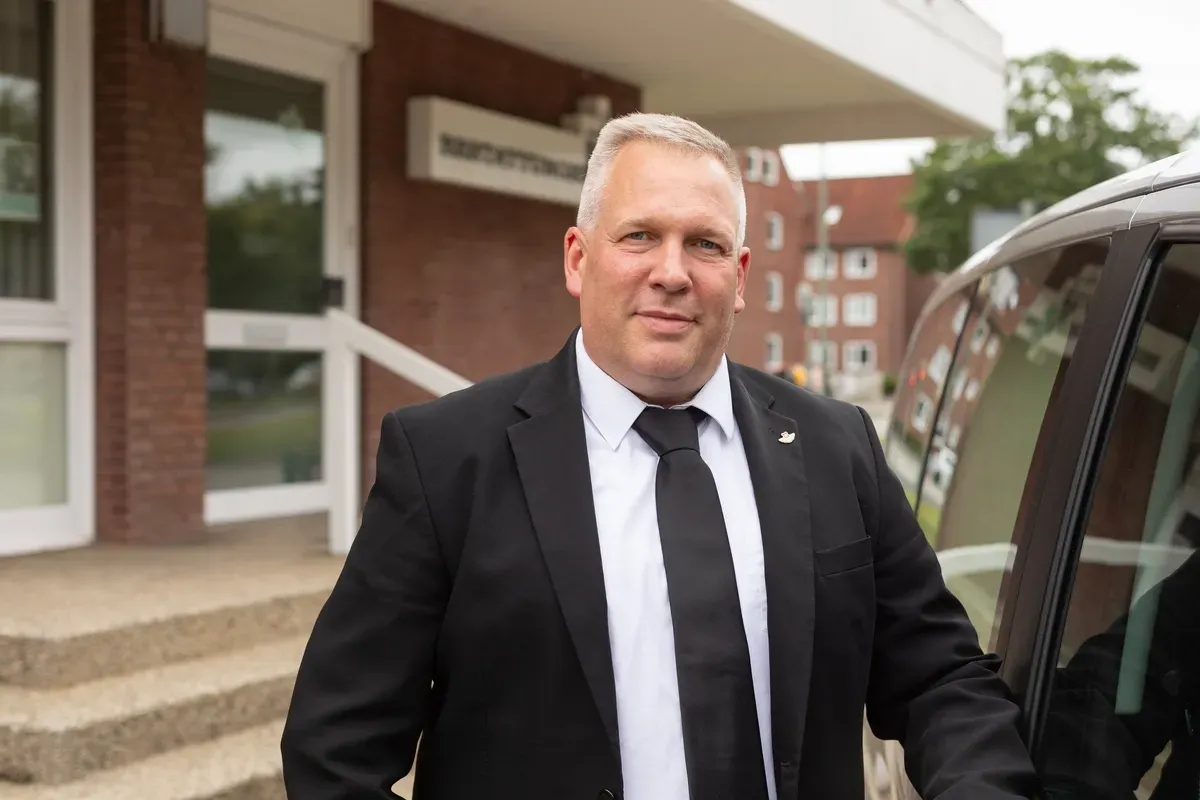 Ein Mann in Anzug und Krawatte steht neben einem Auto.