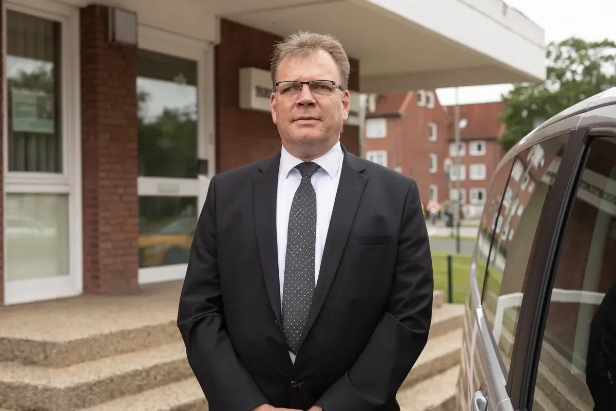 Ein Mann in Anzug und Krawatte steht vor einem Gebäude.