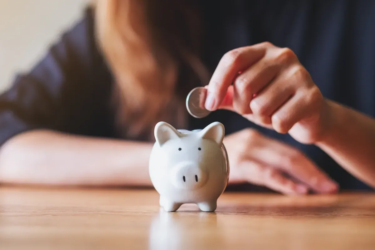 Eine Frau wirft eine Münze in ein Sparschwein.