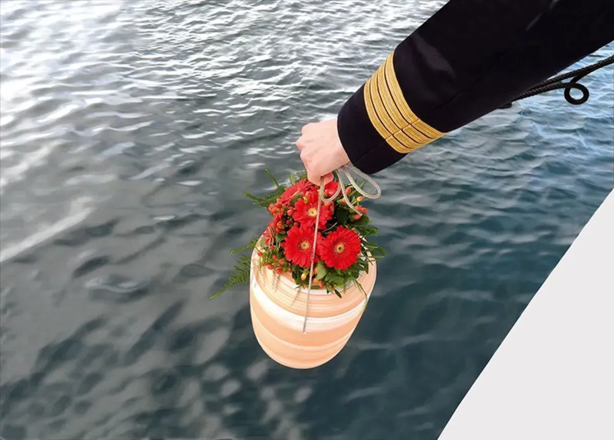 Eine Person hält einen Urne mit Blumen im Wasser