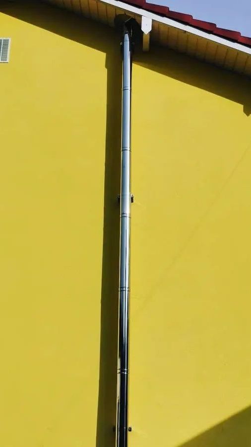 Tuyau d'évacuation des fumées sur un mur extérieur jaune.