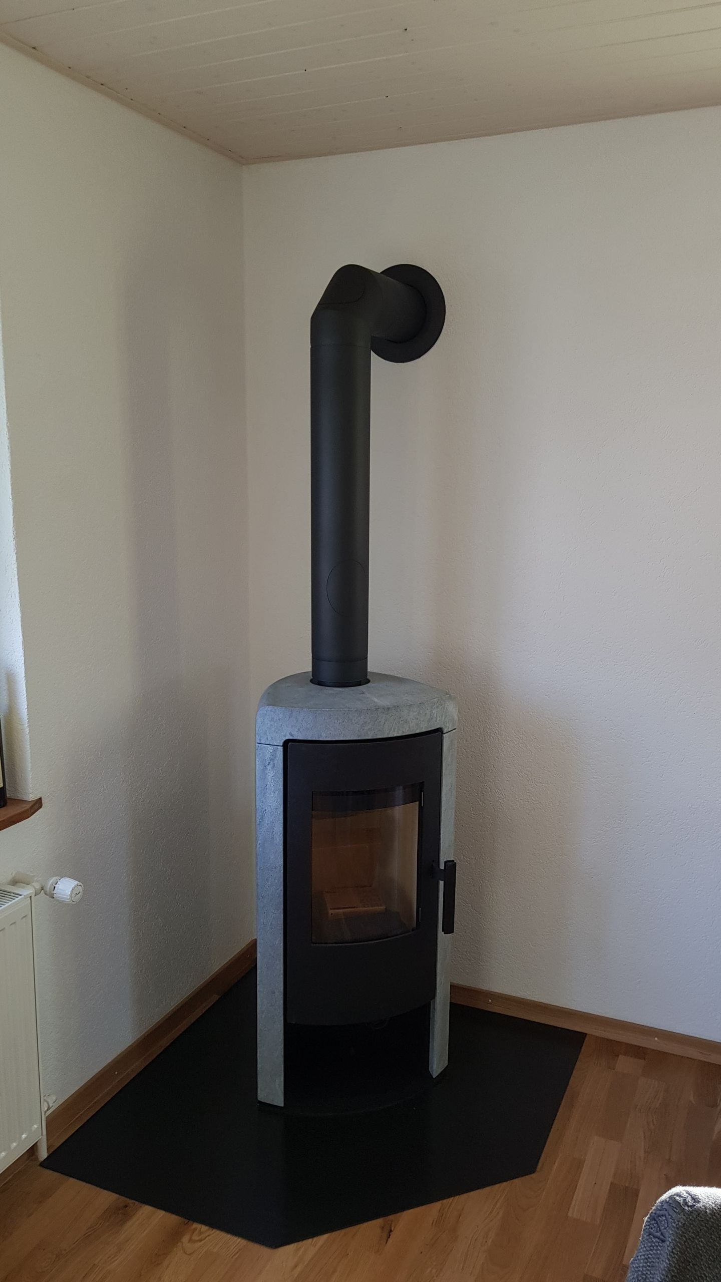 Poêle à bois noir et gris, installé dans l'angle d'une pièce.