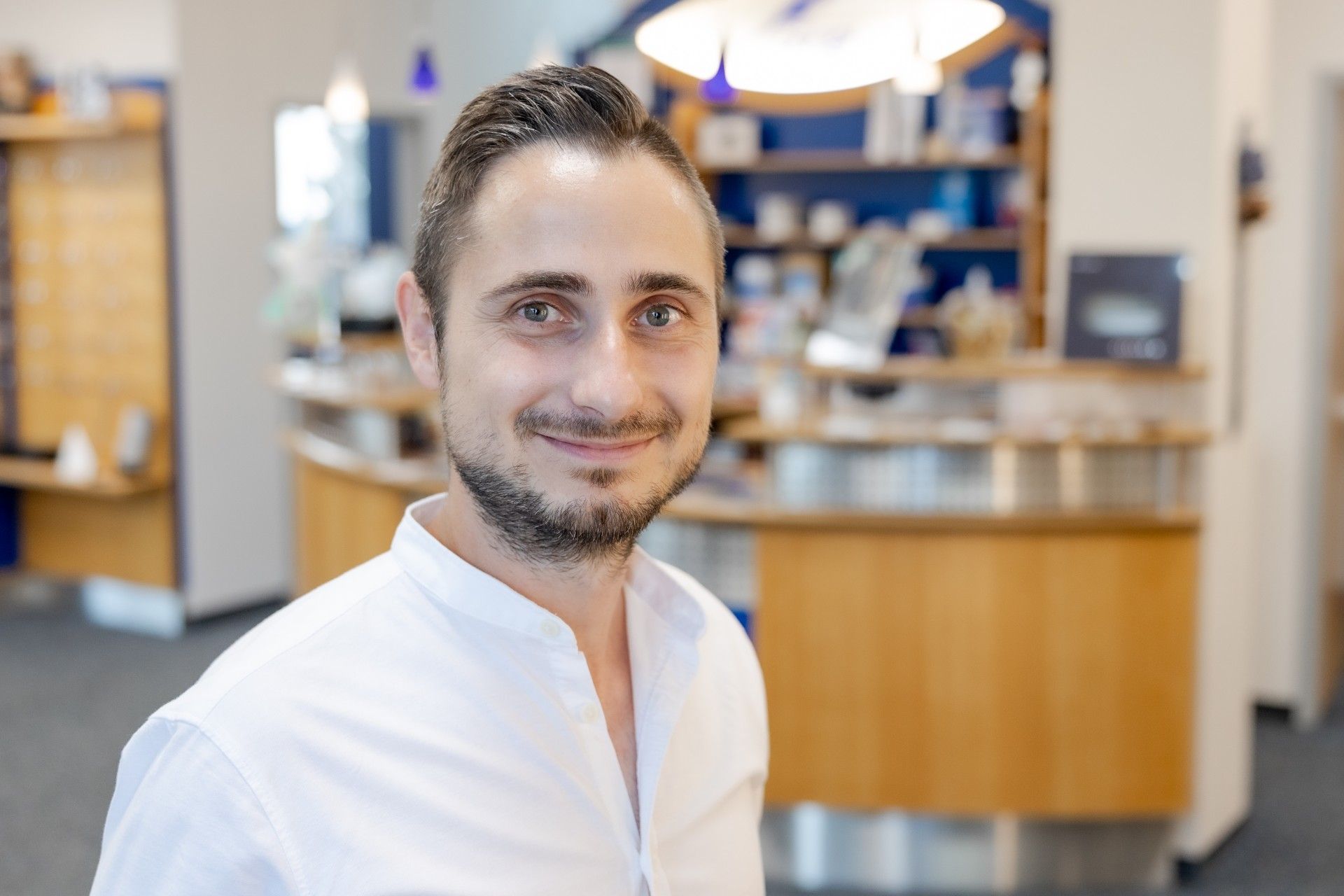 Ein Mann mit Bart steht vor einem Tresen in einer Apotheke.