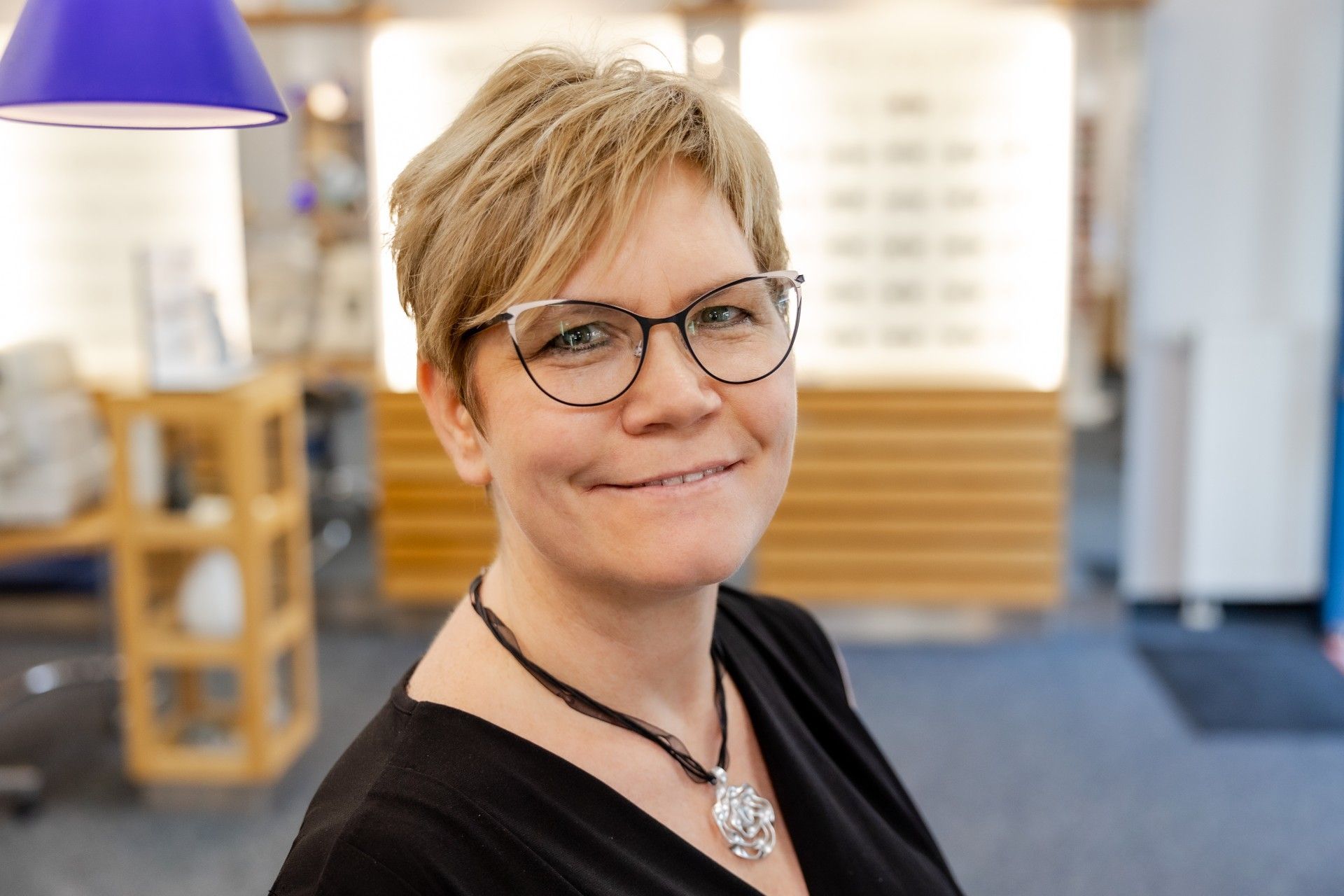 Eine Frau mit Brille und Halskette lächelt in die Kamera.