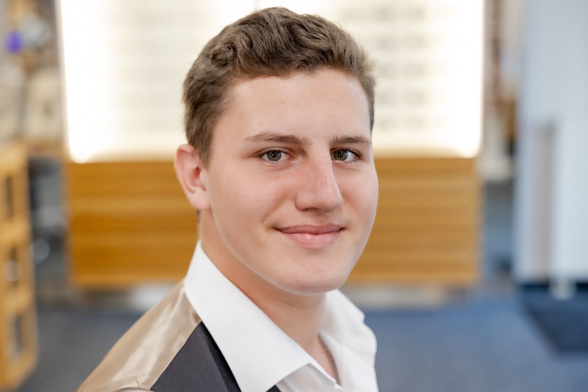 Ein junger Mann in Anzug und weißem Hemd lächelt in die Kamera.