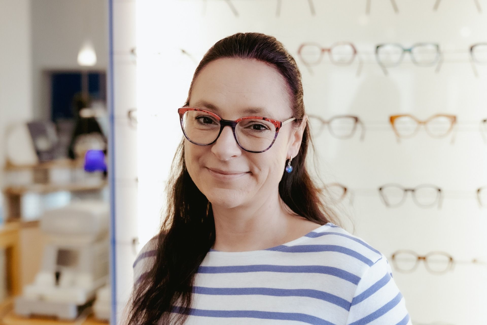 Eine Frau mit Brille steht vor einer Wand aus Brillen.