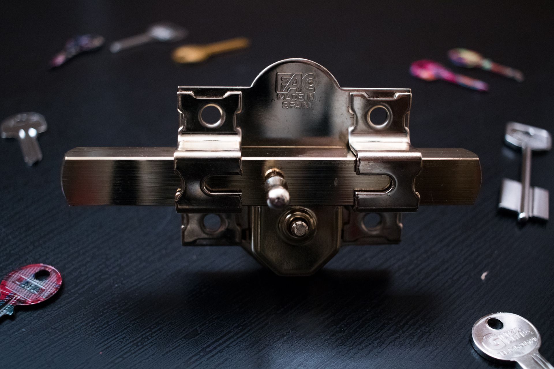 Una cerradura está rodeada de llaves sobre una superficie negra.