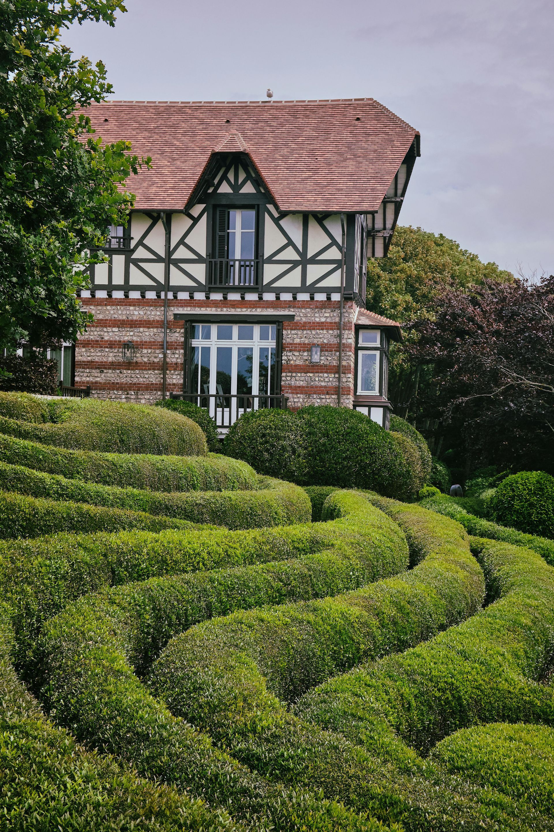 Casa con estructura de madera detrás de setos verdes y arbustos sinuosos.