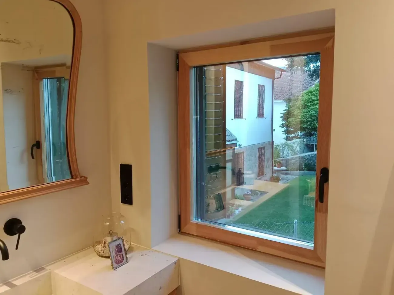 Lavabo y espejo junto a una ventana con vistas a un pequeño patio y césped.