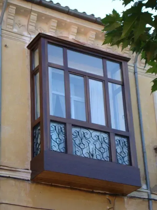 Ventanal azul con balcón decorativo de hierro forjado en la fachada de un edificio de color beige.