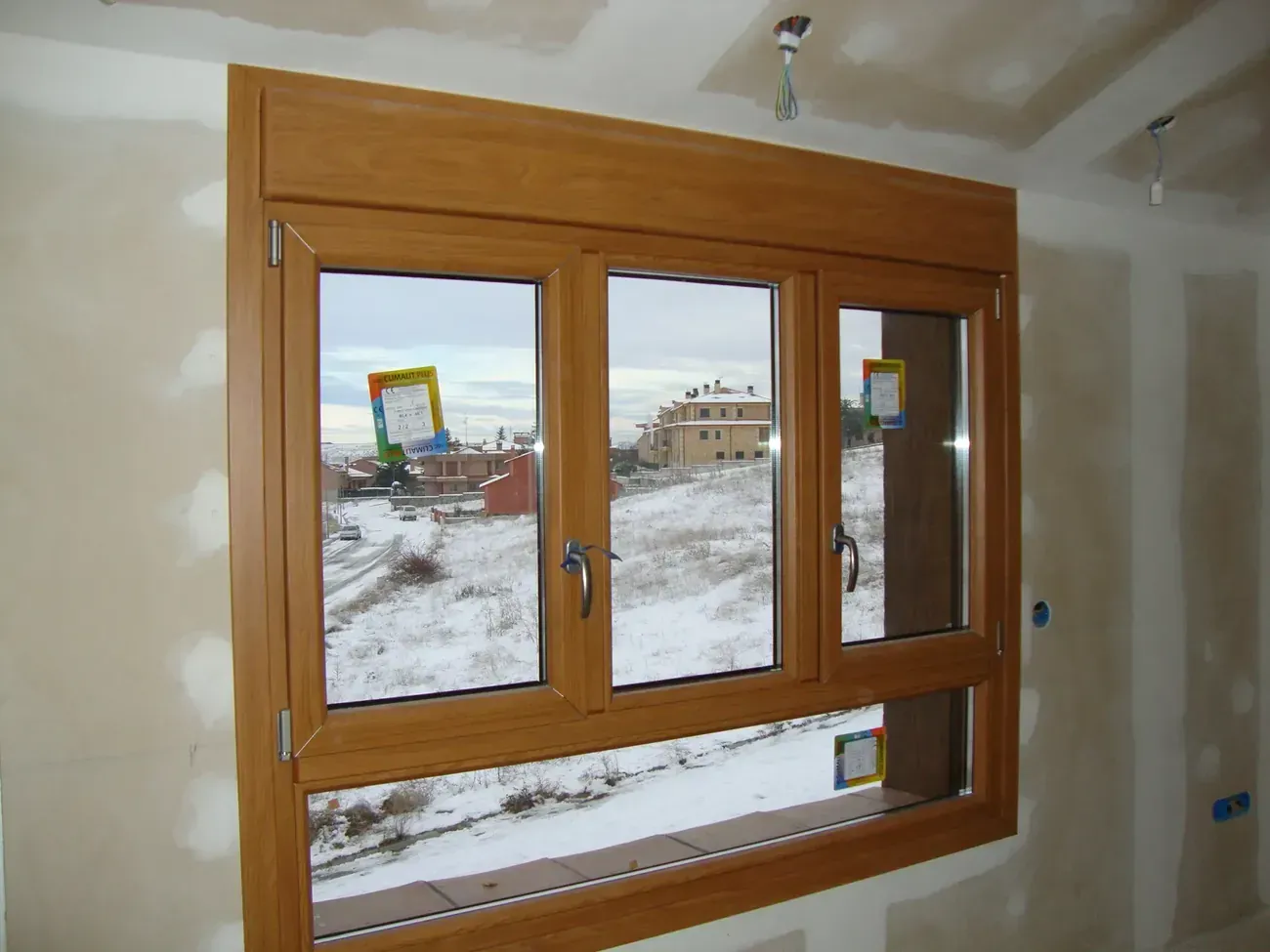Ventana con marco de madera, vista al exterior nevado y un panel inferior parcialmente abierto.