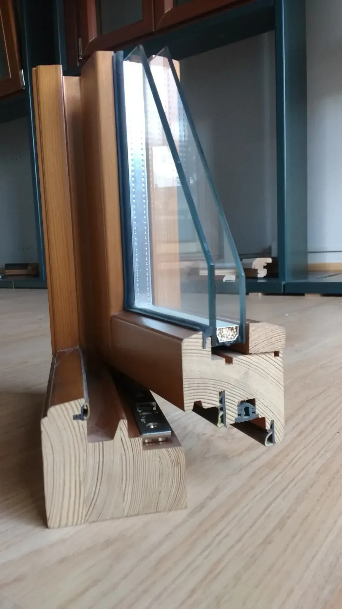 Primer plano de un marco de ventana de madera y sus herrajes sobre un suelo de madera clara.