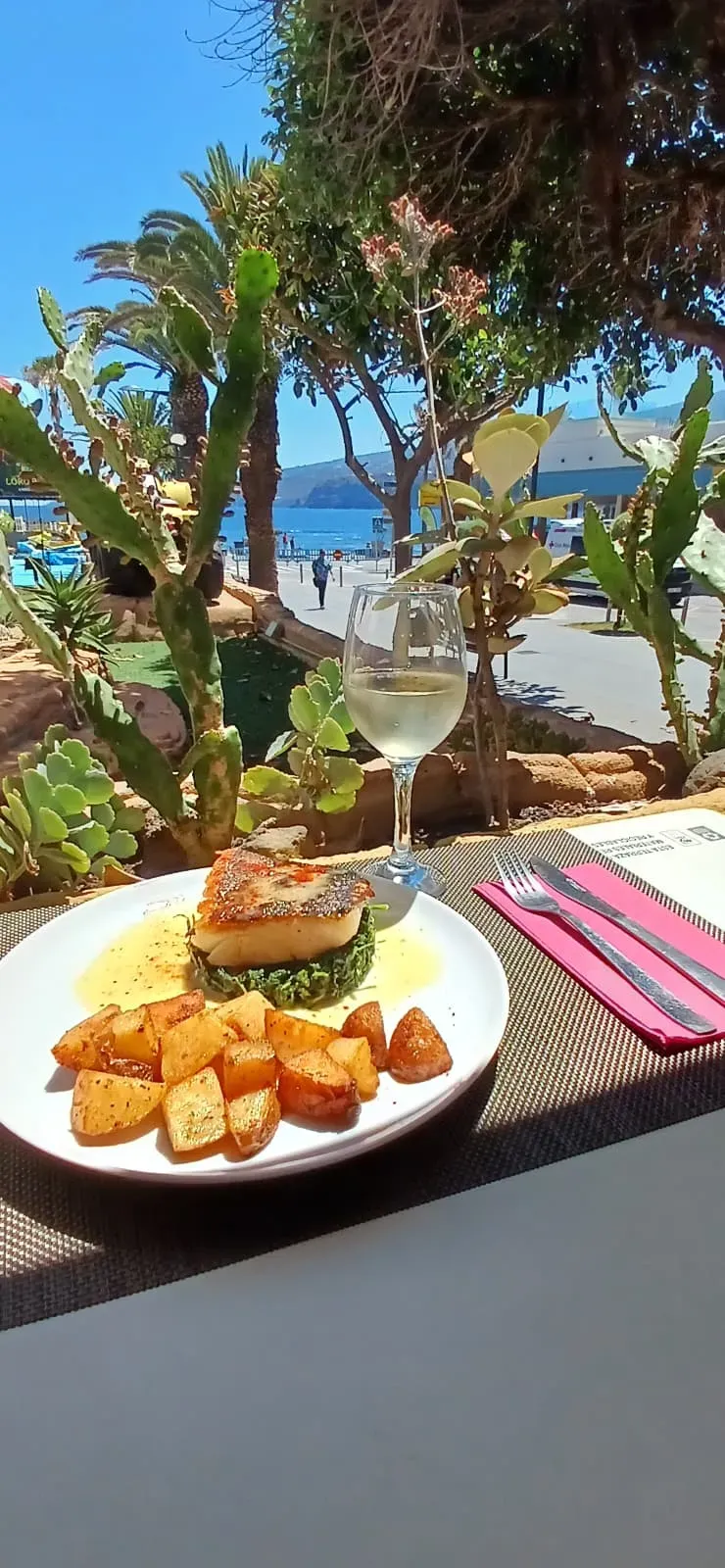 Plato de pasteles y una bebida en una mesa con vistas a una soleada playa tropical y al océano.